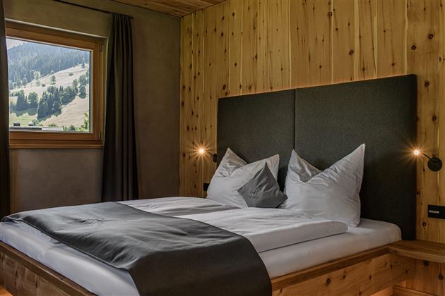 A cozy bedroom with a double bed and wooden paneling. Large windows provide a view of the surrounding nature.