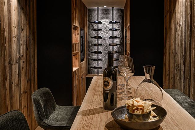 A stylish wine cellar with wooden panels and a long counter. On the counter are a bottle of wine, glasses, and snacks.