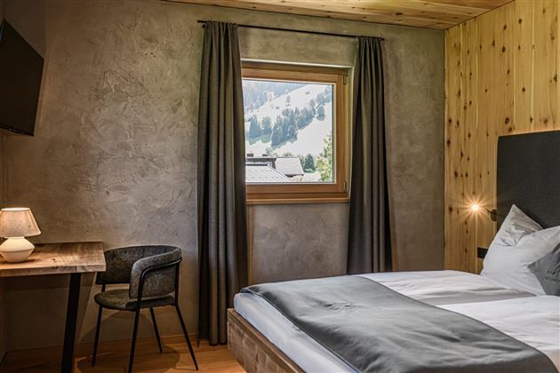 A modern bedroom with a cozy bed and a table. Through the window, one can see the snow-covered mountains.
