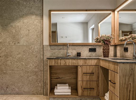 A modern bathroom with wood and stone accents. Two mirrors and an elegant flower vase give the room a stylish ambiance.