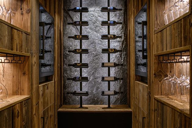 An elegant wooden wine cellar with modern shelves. The wall is adorned with stone, and there are glasses on the shelves.
