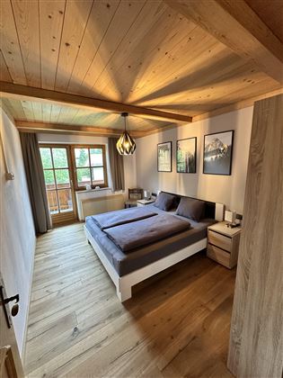 A cozy bedroom with a large bed and wooden floor. A window overlooking nature and decorative pictures on the wall give the room a warm atmosphere.