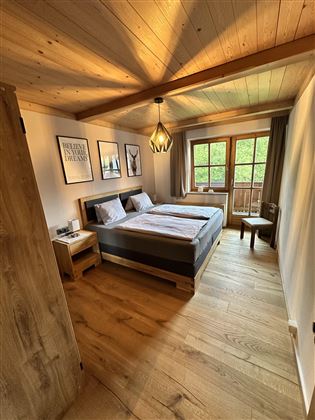 A cozy bedroom with wooden furniture and a large window. The warm colors create an inviting atmosphere.
