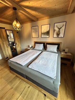 A cozy bedroom with a double bed and wooden decor. Decorative pictures hang on the walls, and the room has a warm, inviting atmosphere.