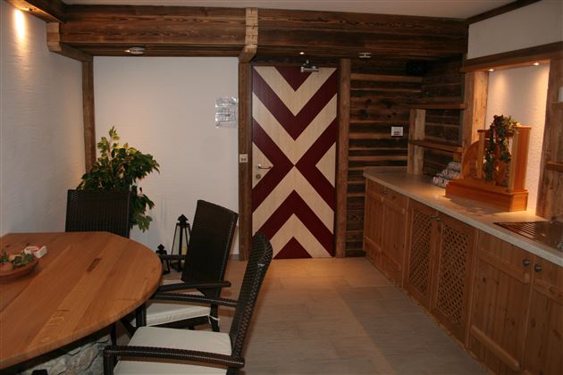 A cozy interior with a round wooden table and chairs. The walls are made of wood, and there is a striking door with a red and white pattern.