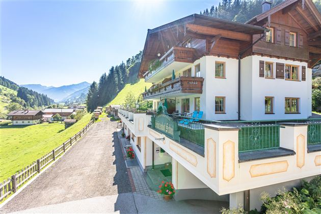 A modern building in the mountains with balconies and a beautiful view. The surroundings are green and sunny, ideal for a vacation in nature.