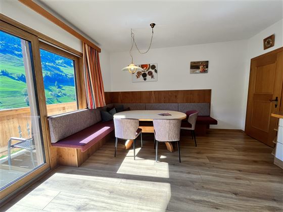 Ein heller Essbereich mit einem runden Tisch und mehreren Stühlen. Große Fenster bieten einen Blick auf die grüne Landschaft.