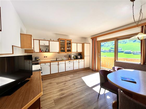 Eine moderne Küche mit Holzschränken und einer großen Fensterfront. Der Raum ist hell und einladend, mit einem Esstisch und schönen Ausblick ins Grüne.