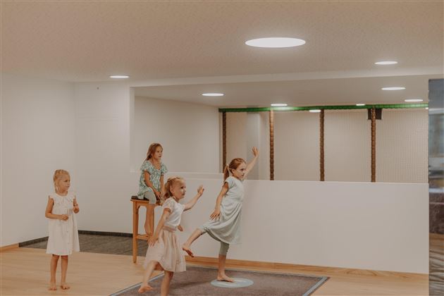 Ein heller, moderner Raum mit vier Mädchen, die spielen und Spaß haben. Die Wände sind weiß und das Licht ist freundlich und einladend.