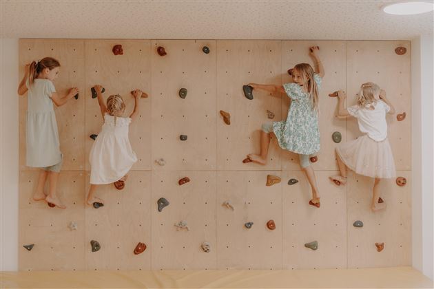 Vier Kinder klettern an einer Kletterwand. Sie tragen verschiedene, sommerliche Kleider und haben viel Spaß.