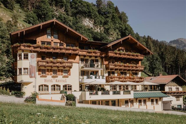Ein charmantes Hotel im alpine Stil, umgeben von grünen Wäldern. Die Fassade ist mit Holzverkleidungen und Balkonen geschmückt.