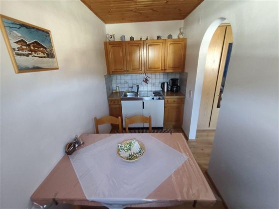 Eine gemütliche Küche mit Holzmöbeln und einem kleinen Essbereich. Der Tisch ist mit einer Tischdecke gedeckt und es sind einige Utensilien sichtbar.