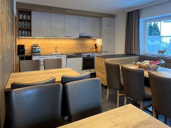A modern kitchen with wood decor and bright lighting. A dining table with chairs is visible in the foreground.