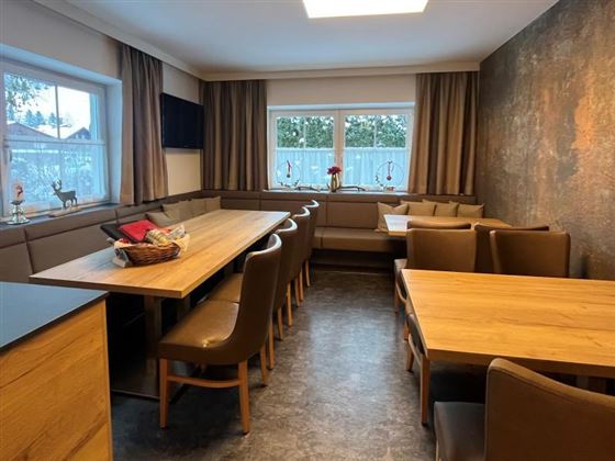 A cozy dining area with wooden furniture and comfortable chairs. Large windows provide plenty of daylight.