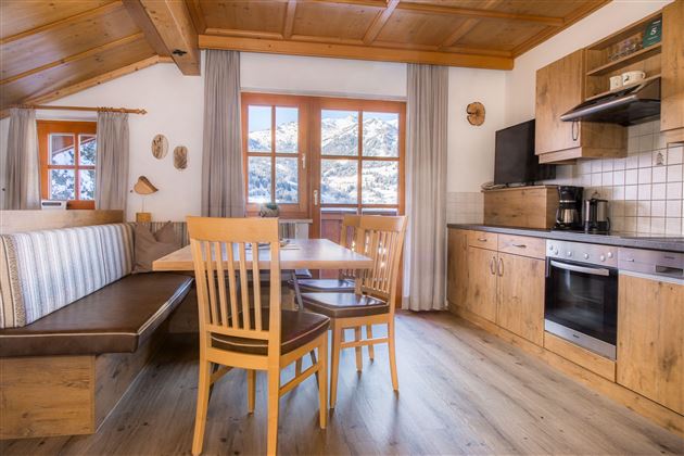 A cozy apartment with wooden furniture and large windows. The room features a dining set and a modern kitchen.