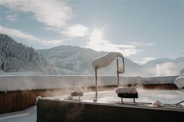 A relaxing outdoor pool in a snowy landscape. The sun shines over the mountains, creating a magical atmosphere.