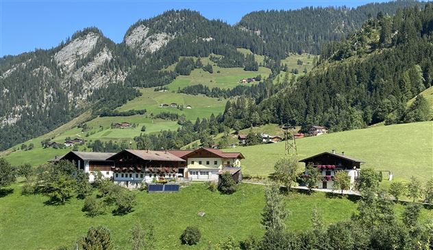 Eine malerische Landschaft mit traditionellen Hütten, umgeben von grünen Wiesen und Bergen. Der Himmel ist klar und die Natur ist sehr einladend.