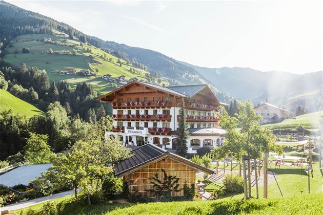 A picturesque hotel in the mountains, surrounded by green meadows and trees. The sun is shining, creating an inviting atmosphere.