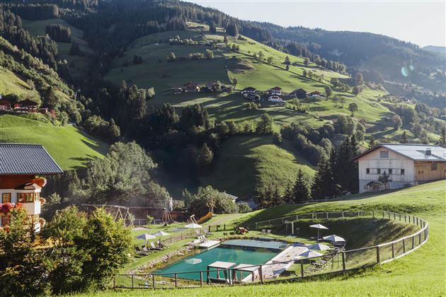 Eine schöne Landschaft mit grünen Hügeln und einem Swimmingpool. Im Hintergrund sind einige Häuser und Bäume zu sehen.