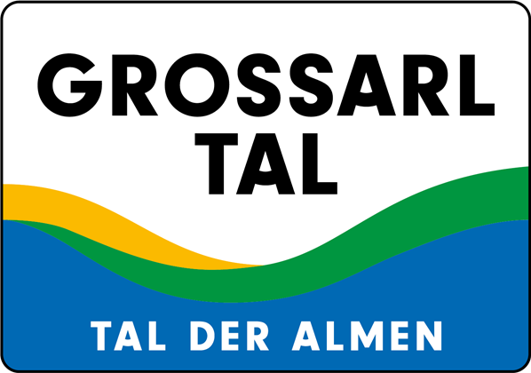 A sign with the inscription "Grossarltal - Valley of the Alps". It displays curved lines in the colors yellow, green, and blue.