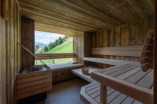 Eine gemütliche Sauna aus Holz mit Blick auf grüne Hügel. Die Bänke sind einladend und die Atmosphäre ist entspannend.