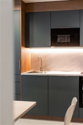 A modern kitchen with dark blue cabinets and wooden details. The space is well-lit and has an elegant, contemporary atmosphere.