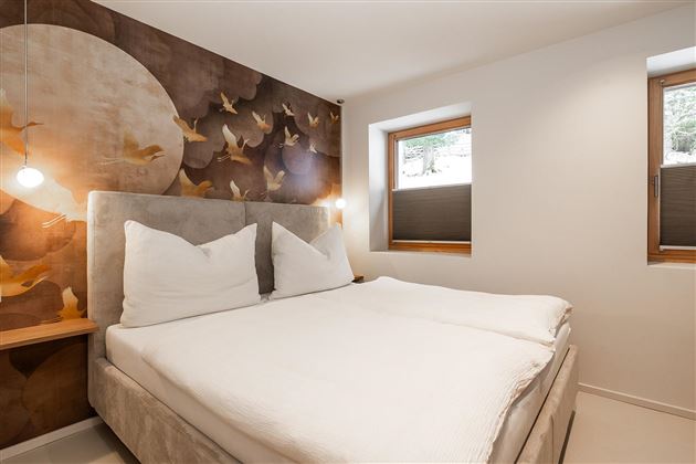 A modern bedroom with a double bed and large windows. The walls are decorated with a stylish bird motif arrangement.