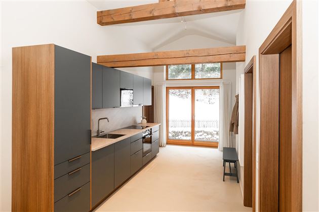 A modern kitchen with wood and gray tones. Large windows allow plenty of light in and provide a view of the structured exterior.