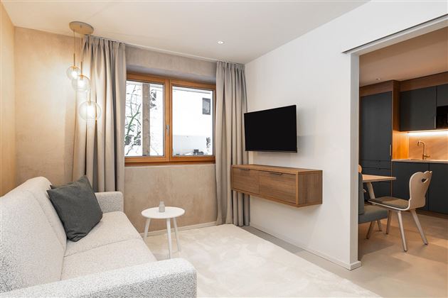 A modern living and dining room with a white sofa and a small table. Large windows provide plenty of daylight and a cozy atmosphere.