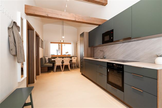 A modern kitchen with dark cabinets and a light countertop. In the background, there is a cozy dining area with wooden chairs.