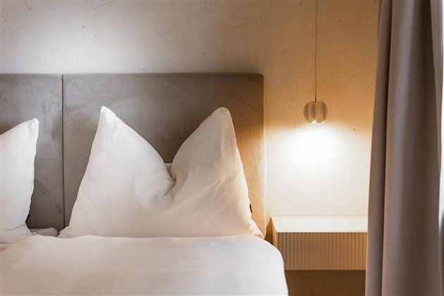 A modern bedroom with a large bed and two big, white pillows. A stylish lamp hangs on the wall, providing soft light.