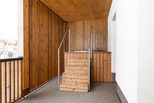 A bright entrance area with a wooden staircase. The walls are adorned with wooden paneling and white plaster.