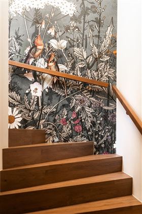 A wooden staircase with a handrail, next to which is a wall adorned with botanical wall design and birds. The background is kept in soft colors and features a variety of flowers.