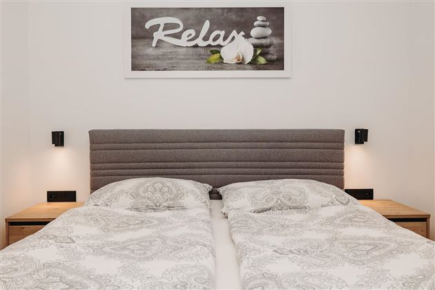 A modern bedroom with a double bed and elegant bedding. A picture with the inscription "Relax" hangs on the wall.