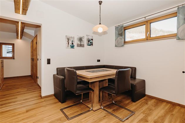 A cozy dining area with a wooden table and modern chairs. The walls are light and there are windows with curtains that let in a lot of light.