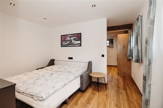 A bright bedroom with a comfortable bed and a small table. The walls are painted in neutral colors and there is a window with curtains.