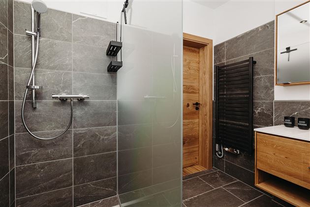 A modern bathroom with an elegant glass shower and gray tiles. Wood details and a sink give the room a warm atmosphere.