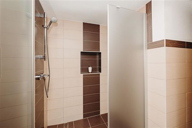 Modern shower with clear glass partitions. The walls are designed with light and dark tiles.