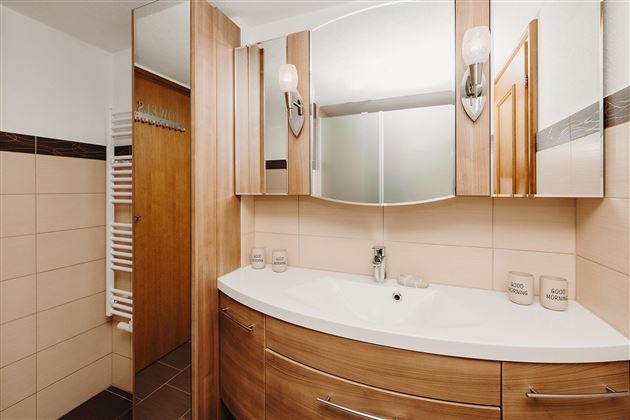 A modern bathroom with wood and tile accents. It features a curved sink and large mirrors.
