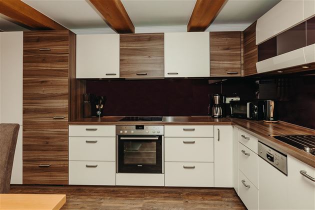 A modern kitchen with white and dark wood cabinets. It is equipped with an oven, a cooktop, and various kitchen appliances.