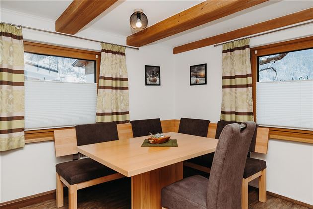 An inviting dining area with a large wooden table and elegant chairs. The large windows let in plenty of daylight and offer a view outside.
