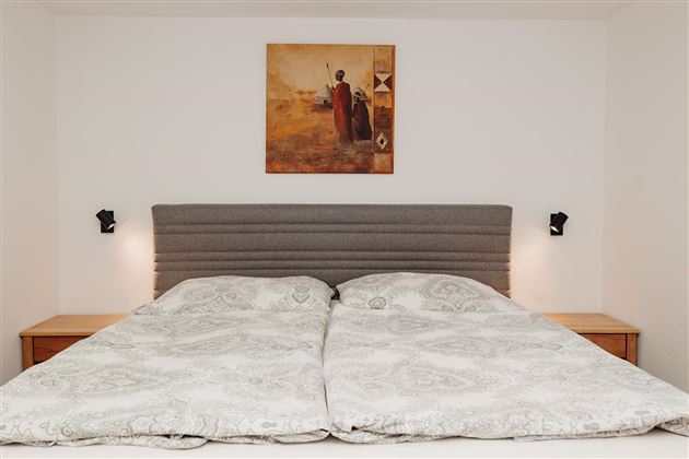 A cozy bedroom with a large bed and a neutral color scheme. A decorative picture hangs on the wall.
