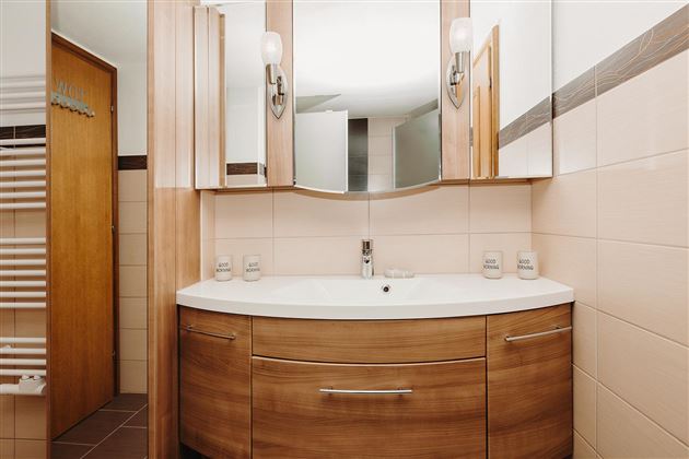 A modern bathroom with wooden cabinets and a sink. The walls are bright tiled and there are large mirrors above the sink.