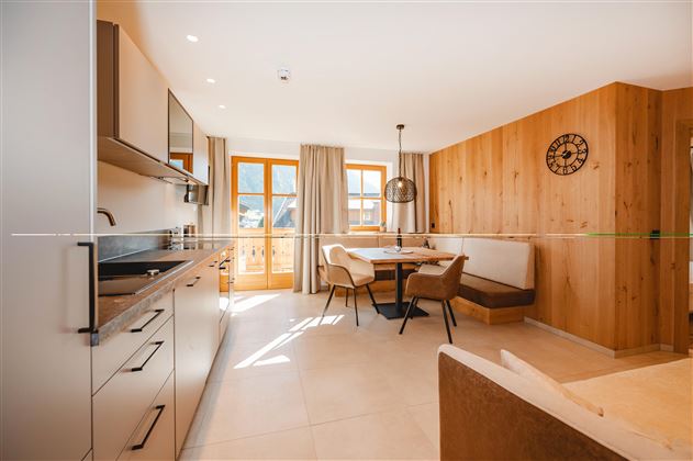 A modern kitchen with wooden details and a dining area. Large windows provide plenty of natural light.