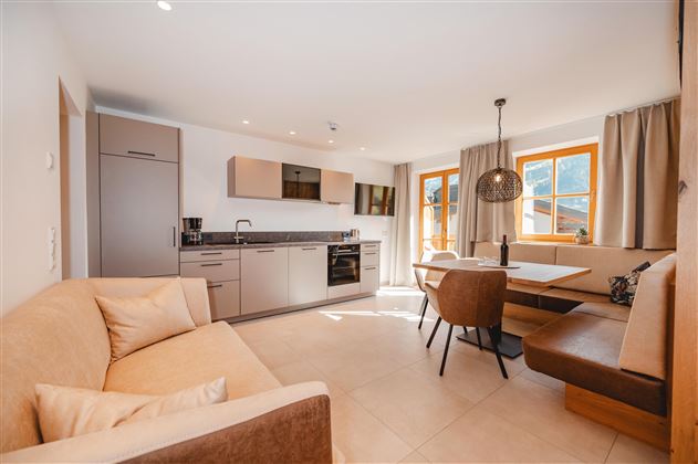 A modern kitchen with a comfortable dining area and large windows. The space is bright and friendly with contemporary furnishings.