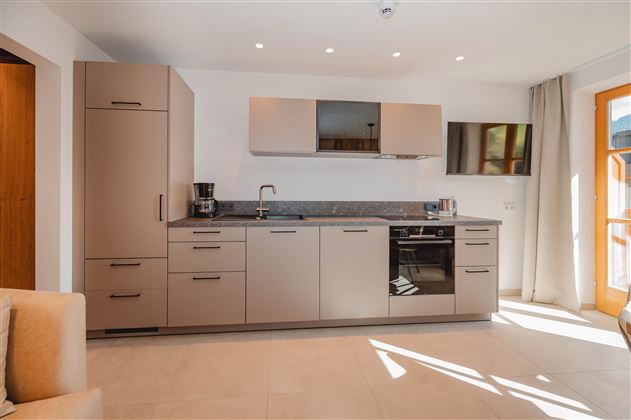 A modern kitchen with light cabinets and an elegant countertop. The room is well-lit and has large windows.