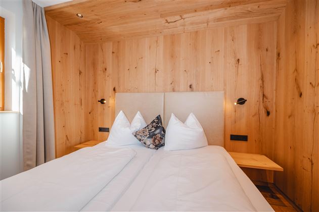 A cozy bedroom with a double bed and wooden walls. Bright colors and a pleasant atmosphere can be seen.