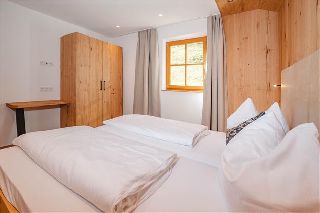 A cozy bedroom with a double bed and wooden furniture. Large windows let in plenty of natural light.