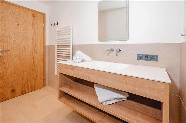 A modern bathroom with a wooden washbasin and a large mirror. Fresh towels are neatly arranged on the shelf.