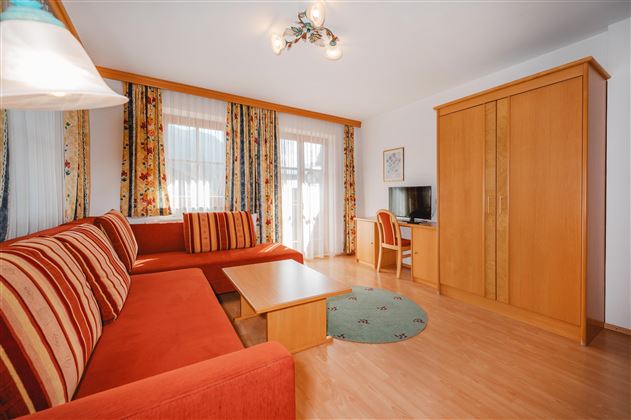 A cozy living room with a red sofa and a wooden table. Large windows provide plenty of light and an inviting atmosphere.